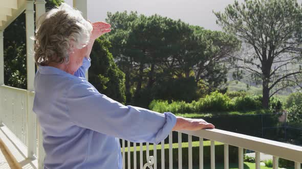 Smiling caucasian senior woman at home enjoying view of sunny garden from balcony