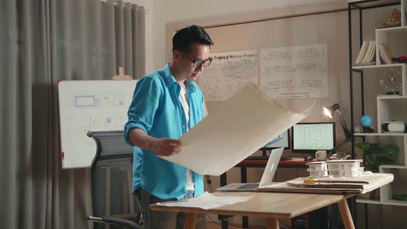 Asian Man Engineer With A Laptop Looking At Blueprint While Working At The Office