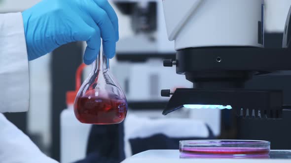 Scientist Mixing Pink Liquid in the Glass Flasks