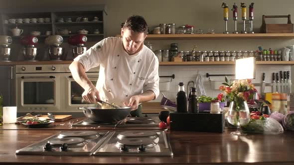 Chef in a restaurant uniform is stirring spaghetti with tongs. Cooking the pasta