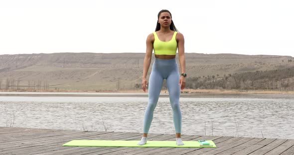 Athletic young woman fitness model warming up doing squats exercise for the buttocks.