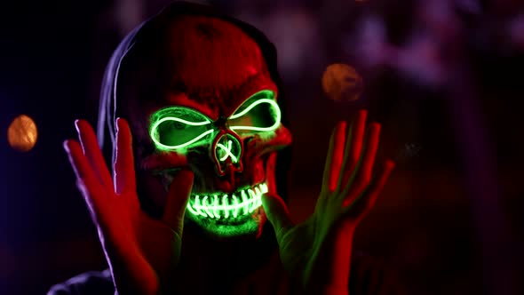 Portrait of a Person in a Glowing Mask of Death and in a Dark Hood on a Blurry Background with