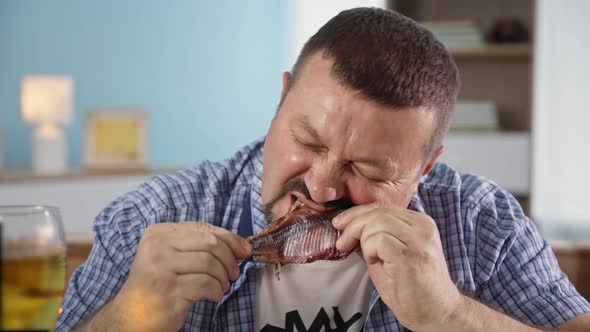 Portrait of a Happy Man Having Fun Eating Fish and Beer While Relaxing After Work at Home