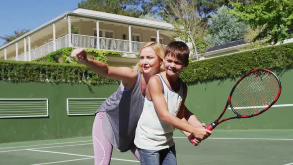 Caucasian mother teaching her son to play tennis at tennis court on a bright sunny day