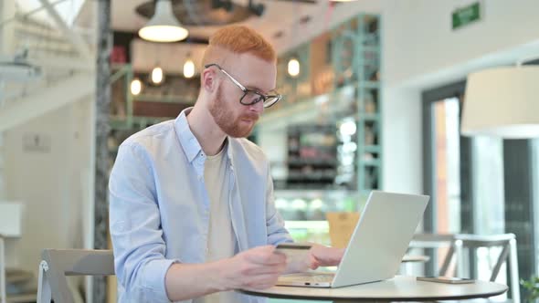Redhead Man Cheering Online Payment Success on Laptop in Cafe
