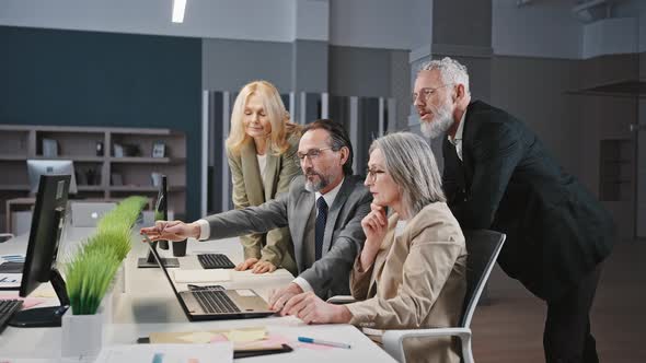 Professional Mature Man Employee Showing Plan on Laptop to Colleagues Discussing Project at Office