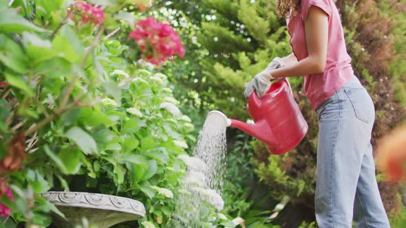 Happy biracial woman gardening, watering plants with watering can