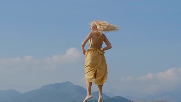 Dancing blonde woman in a yellow dress  against the background of mountains in Montenegro.