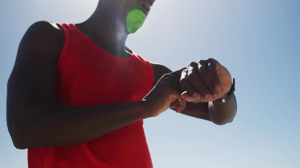 African american man checking his smartwatch, taking break in exercise outdoors by the sea