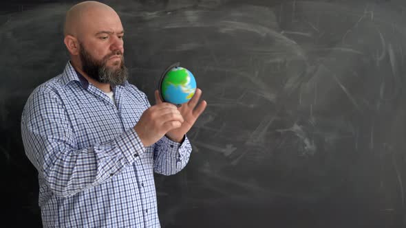 an Adult Bearded Caucasian Man in a Shirt Stands and Rotates the Globe