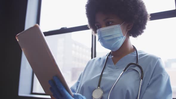 Mixed race female doctor wearing face mask using digital tablet