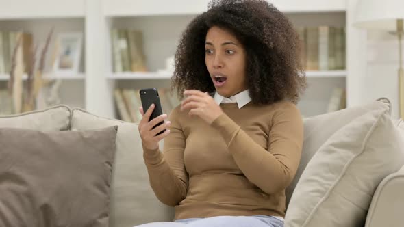 Young African Woman Reacting to Loss on Smartphone on Sofa