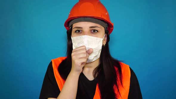 Female Construction Worker in Overalls and Medical Mask Coughing on Blue Background