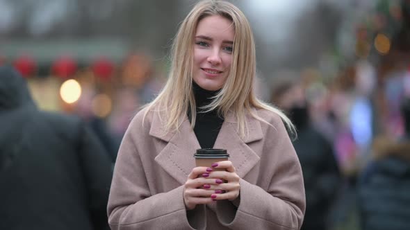 young girl in a coat standing on street and holding cup of hot drink