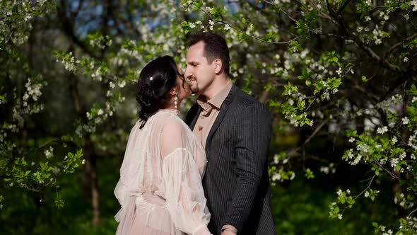 Happy Married Couple is Standing in Blooming Garden in Spring Day Husband is Kissing His Wife