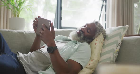 Video of sad african american senior man laying on sofa