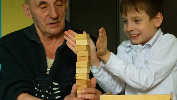 Caucasian grandfather 70 years old with his grandson 7 years old play fun at home, build a tower of