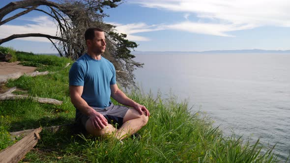 A fit man sitting in a meditation pose practicing deep breathing and mindfulness exercises on a beac