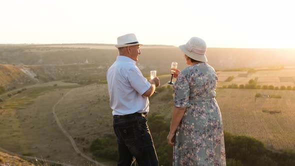 Elderly Couple on the Top of the Hill, Cheer Glasses of Champagne at the Sunset.