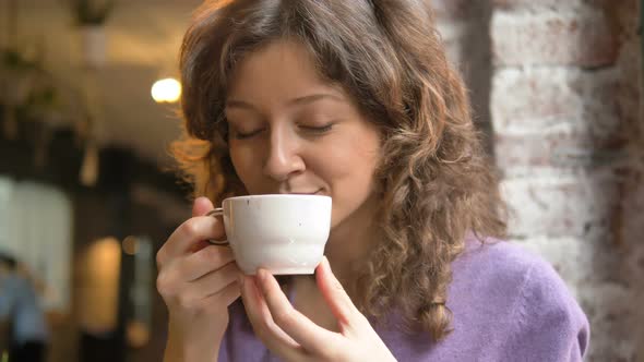 Young Woman Holds White Ceramic Cup and Enjoys Coffee Smell