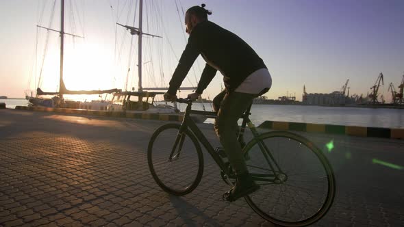 Stylish Handsome Man Riding Bicycle During Sunset or Sunrise with Sea Port on Background Slow Motion