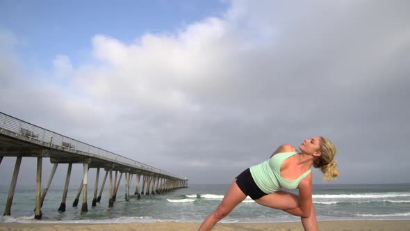 A young attractive woman doing yoga on the beach next to a pier