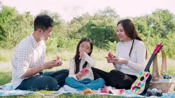 Happy family picnic. Asian parents (Father, Mother) and little girl eating watermelon and have fun