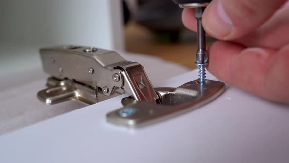 Carpenter Man Screws Hinge to Furniture Door Using Electric Screwdriver Hands Closeup View