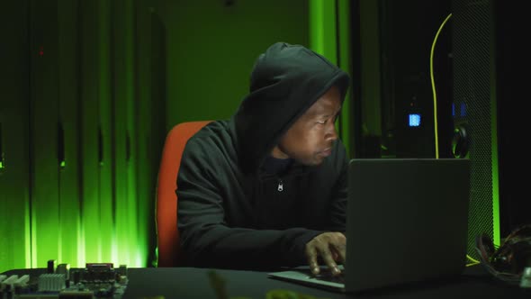 African american male computer hacker using laptop in business server room