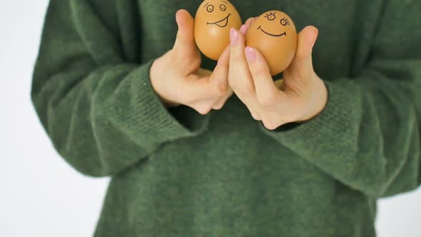 Young Female in Green Sweater is Showing Eggs with Hand Drawn Face with a Smile From Straw Basket