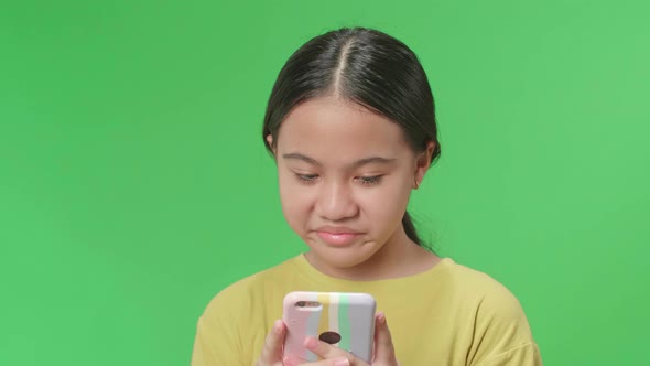 Asian Kid Girl Emotionally Flipping Something On The Phone While Standing In The Green Screen Studio