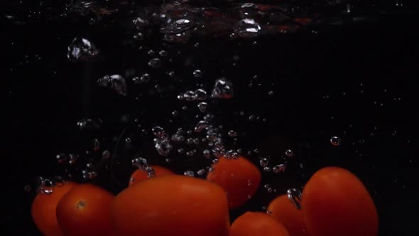 Red Tomatoes Fall and Float in Water. Black Background. Slow Motion. Food Video Tomatoes