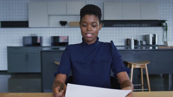 African american businesswoman having video chat going through paperwork in workplace kitchen