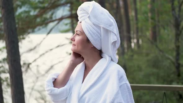 Young Woman in a Bathrobe and Towel on the Terrace on a Background of Mountains and Forest