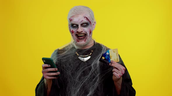 Sinister Man Halloween Zombie Using Credit Bank Cards and Smartphone While Purchases Online Shopping