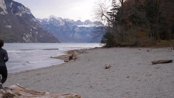 Sporty couple running on the stony shore of a lake in front of a mountain range with snowy peaks