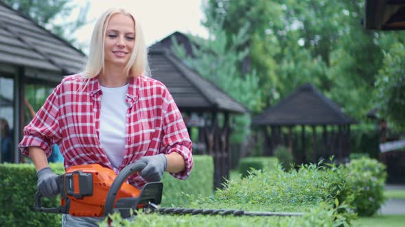 Charming Woman Using Electric Trimmer for Shaping Bushes Outdoors