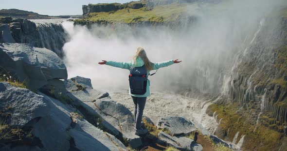 Woman Standing on the Edge of the Cliff and Raising Her Hands Up in the Air Wiht Beautiful Detifoss