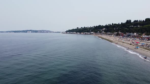 Drone shot contrasting the calm waters of the Puget Sound and the busy sands of Alki Beach in Seattl