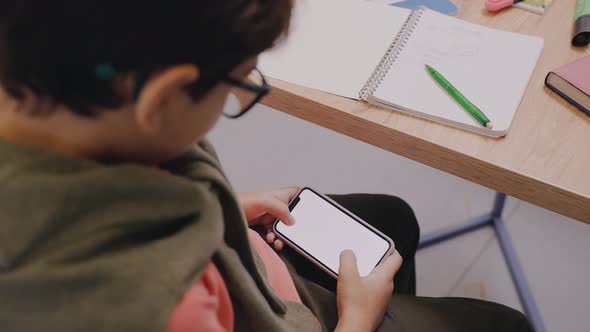 Boy is Playing Mobile Games at the Break Sitting at the Desk