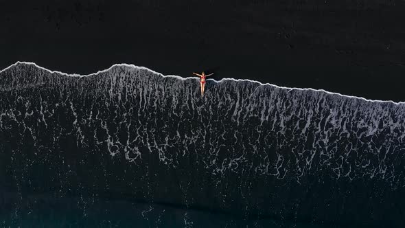 Top View of a Woman in a Red Swimsuit Lying on a Black Beach on the Surf Line. Coast of the Island