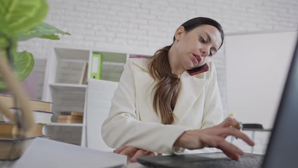 Bottom View of Busy Confident Woman Talking on the Phone Typing on Laptop Keyboard and Writing on