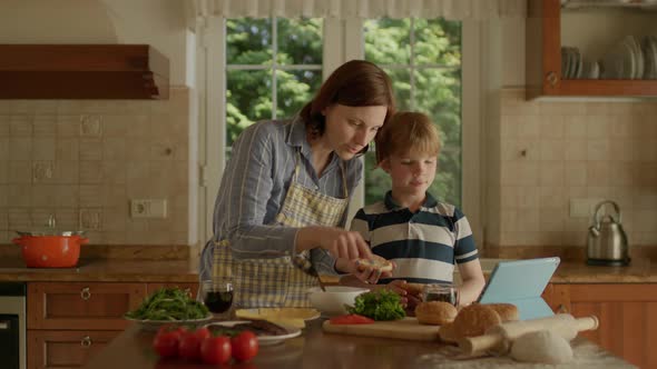 Mother and Son Cooking Burgers at Home Using Tablet Computer for Online Recipe