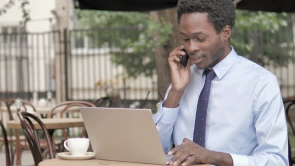 African Businessman Talking on Phone While Sitting in Outdoor Cafe