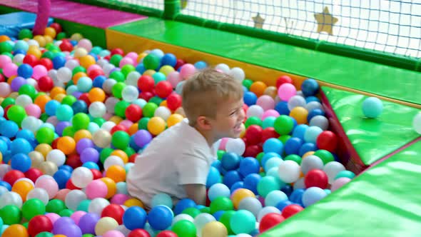 Blonde Little Boy Scatters Balls in Different Sides Lying on Multi Coloured Plastic Balls in Big Dry
