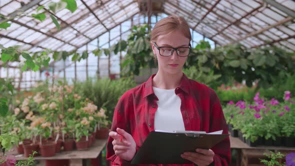 Agronomist Girl in Glasses and Checkered Red Shirt Checks the Quality and Quantity of Plants in the