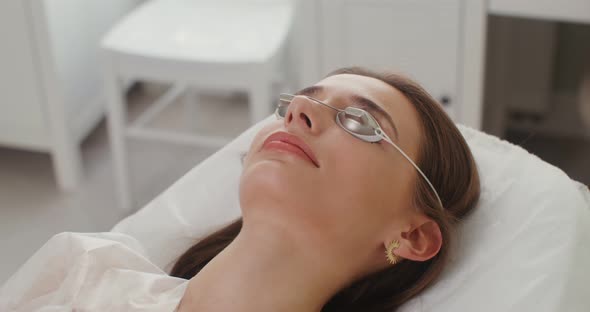 A Woman Patient in Protective Glasses Lies in a Cosmetology Room