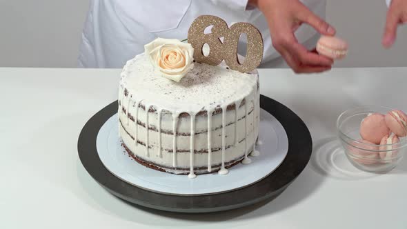 Beautiful Birthday Cake Decorated with Macarons and a Rose Being Proudly Presented By a Female Baker