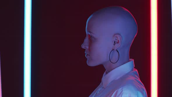 Young Bald Woman Standing between Two Flickering Neon Lamps