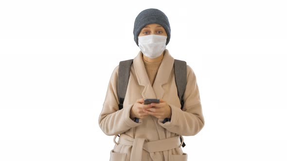 Woman Dressed in a Coat Wearing Medical Mask Using Phone and Walking on White Background